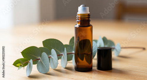 Essential oil roller bottle beside eucalyptus sprig on wooden table  