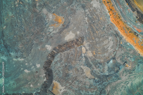 Top-down abstract photograph of industrial tailings or chemical runoff. Unnatural swirling patterns of blue-gray, turquoise, and rusty orange minerals - environmental pollution and contamination.