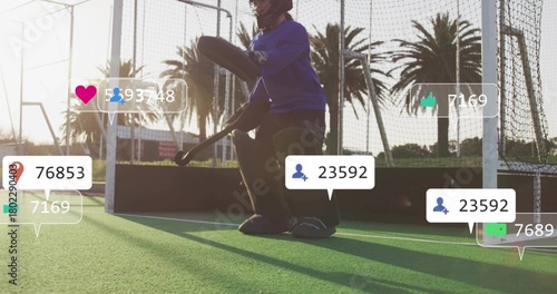 Crouching goalkeeper wearing full pads preparing to save at goal on fenced turf, social overlays