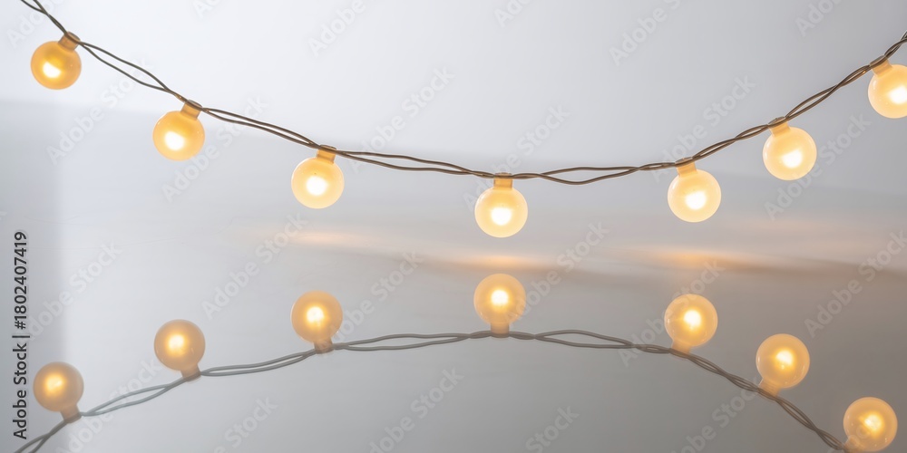 Obraz premium Glowing String Of Round White LED Fairy Lights Or Glimmering Party Globes Draped On A Subtle Reflective Background For Decoration And Festive Events