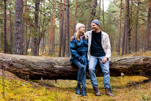 smiling couple sitting and resting on fallen tree after walk in autumn park