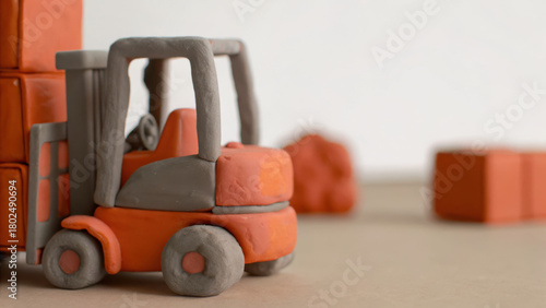 Clay miniature forklift in orange and gray colors with stacked boxes in background showing logistics and transportation concept