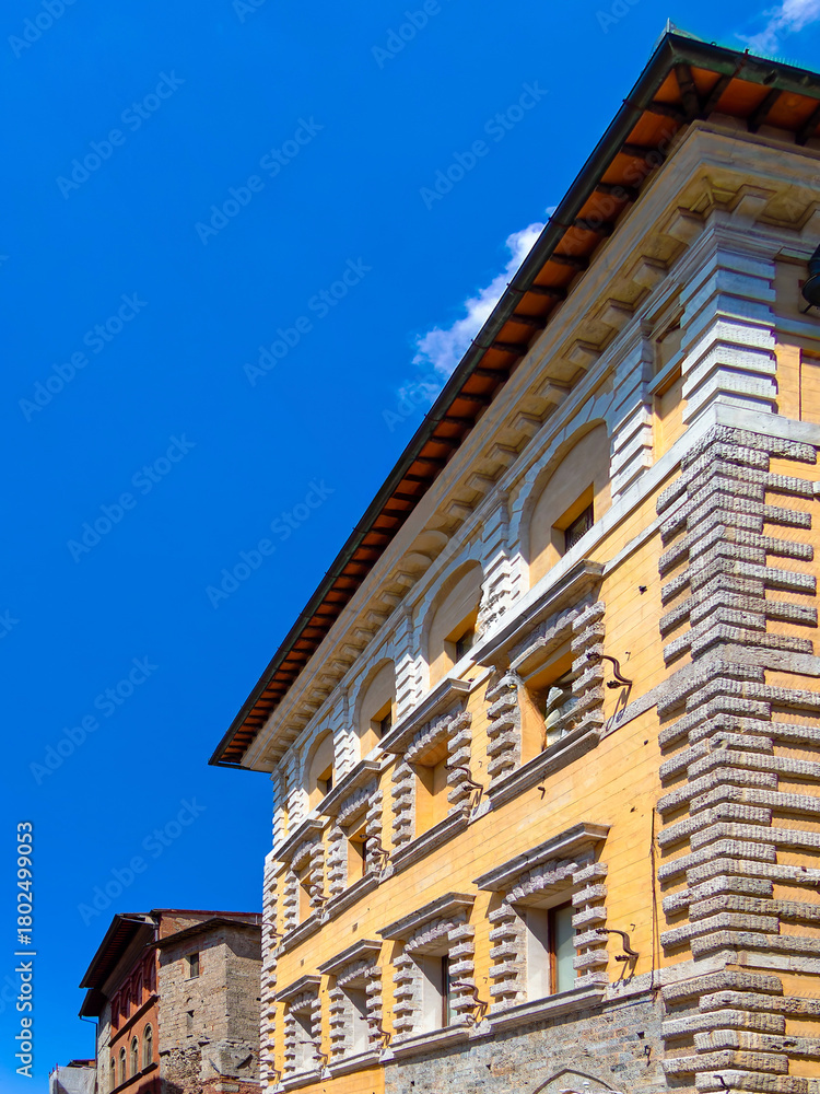 Fototapeta premium Classic vintage buildings stand elegantly under a vibrant blue sky in Siena, Tuscany, Italy, showcasing intricate stone facades, arched windows, and historic charm.