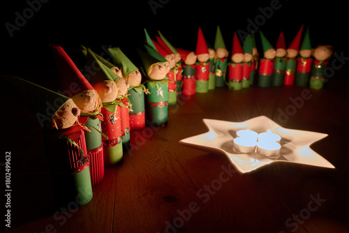 Wichtelfiguren aus Papier als Adventskalender vor einem Sternenteller mit vier Kerzen