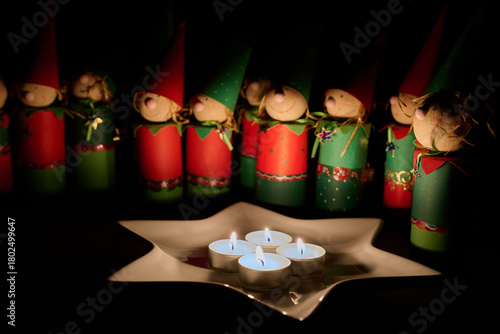 Wichtelfiguren aus Papier als Adventskalender vor einem Sternenteller mit vier Kerzen