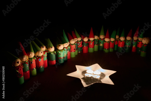 Wichtelfiguren aus Papier als Adventskalender vor einem Sternenteller mit vier Kerzen