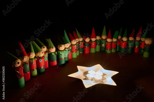 Wichtelfiguren aus Papier als Adventskalender vor einem Sternenteller mit vier Kerzen