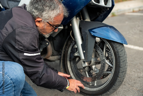 Mature motorcyclist checking front tire of motorcycle