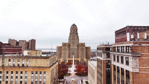 Aerial drone view of downtown Buffalo, New York, featuring a straight-on perspective of a city street lined with tall commercial buildings leading to the iconic Buffalo City Hall. The scene captures u