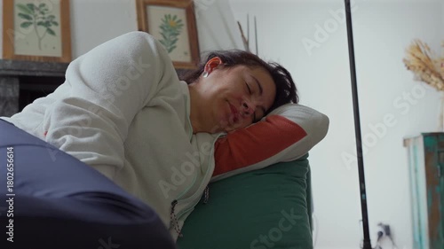 Mother lying on couch yawning widely in soft home light, capturing candid moment of fatigue, rest, and everyday family life with relaxed natural expression during quiet afternoon at home