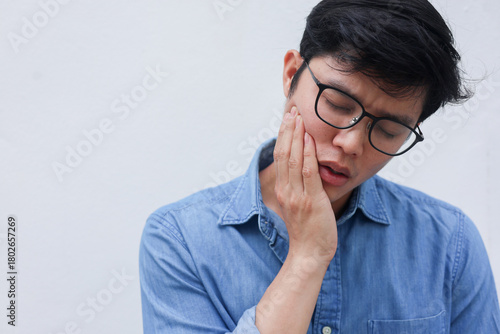 close up young asian man frown and use hand to massage on cheek after feeling pain or hurt from tmj muscle symptom at home for un healthy lifestyle and treatment concept