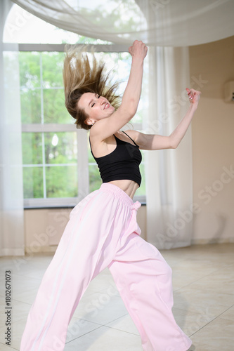 Young woman dancing hip-hop and jazz-funk in studio wearing black crop top, pink pants, with hair flowing. Dance instructor. Contemporary choreography concept. Portrait of athletic girl in motion.