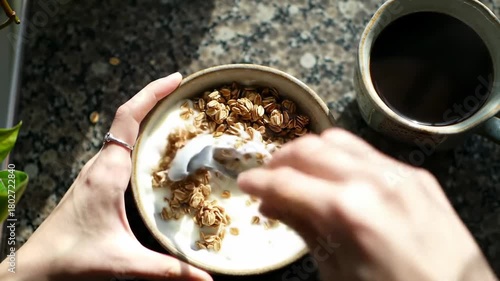 Delicious yogurt bowl with granola and coffee on marble countertop. Yogurt topped with crunchy granola and served with steaming cup of coffee. Concept of healthy breakfast for food enthusiasts.