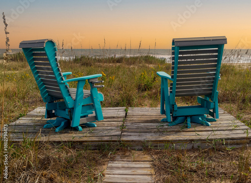 two deck chairs overlooking dunes and ocean at sunset