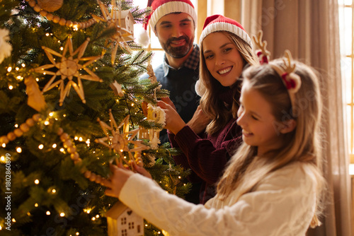 Obraz na plátně Parents and daughter having fun decorating Christmas tree, placing Christmas lig