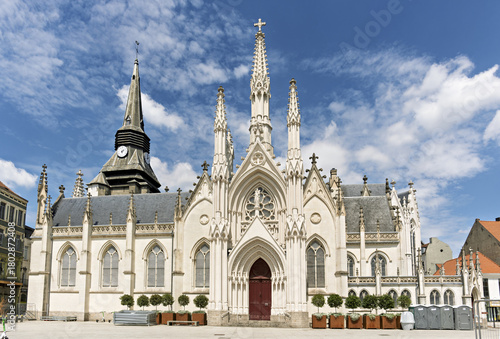 Gothic-style church in Roubaix, France, featuring a symmetrical facade with pointed arches, tall spires, and ornate stone carvings, centered around a large red door
