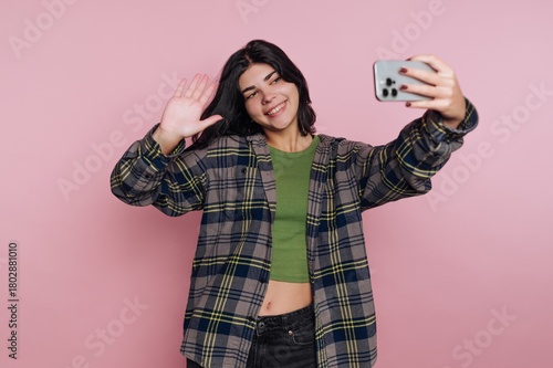 portrait of young woman happily poses for a selfie, showing joy and spontaneity on pink background