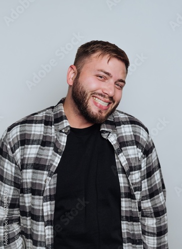 portrait of young joyful man in a checkered shirt flashes a big smile, radiating positivity on white background