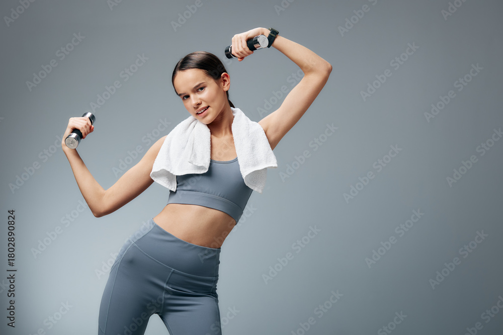 Naklejka premium Woman fitness enthusiast performing an exercise with dumbbells in a gym, towel around neck. Dynamic workout captures movement, strength, balance, core focus, health and motivation in a modern studio.