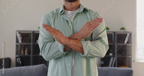 Torso view of man crossing arms into a cross sign, a firm gesture that communicates rejection and stop at home bu hands. He marks boundary to refuse and deny. Clear warning signal in nonverbal form.