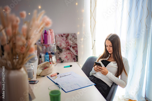 Teenager using phone at desk procrastinating homework