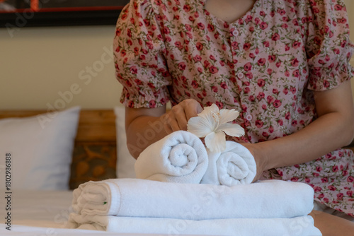 Hands of hotel maid putting plumeria flower and towels on the bed in the luxury hotel room ready for tourist travel