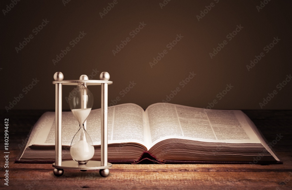 Naklejka premium Sandglass with ancient book. History concept