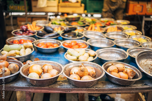 Bowls of onions, tomatoes, potatoes, and eggplants displayed at an outdoor market stall