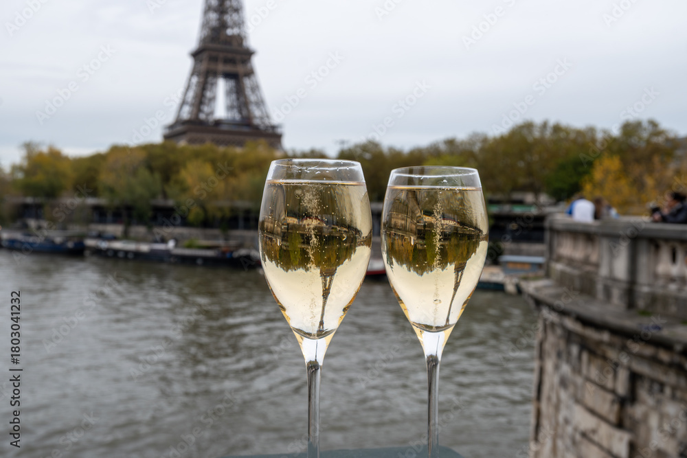 Obraz premium Pouring and drinking of french sparkling wine champagne from tulip glasses with view on Paris streets, buildings, Seine river and towers, wedding event in Paris