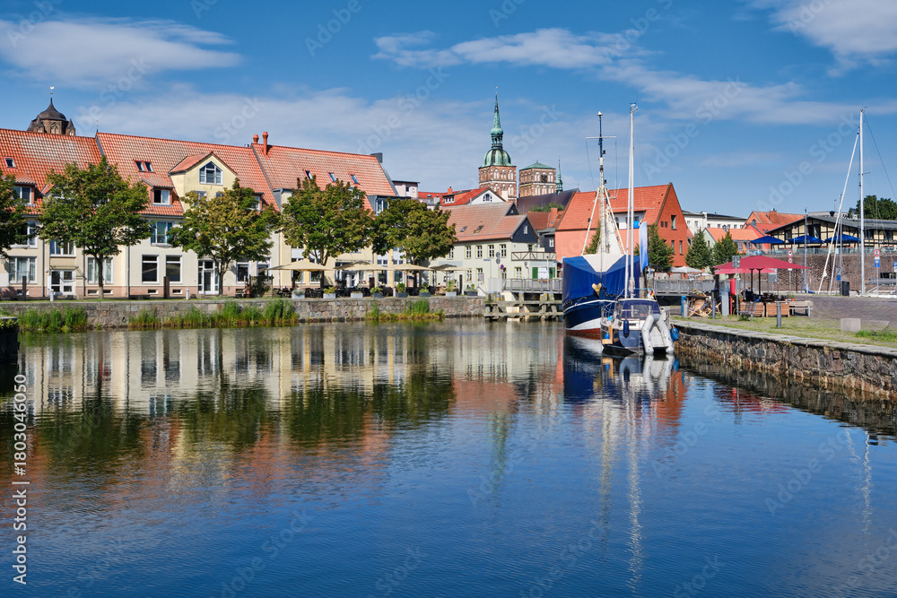 Fototapeta premium Charming view of Stralsund harbor in Germany with boats, historic buildings, waterfront cafes, and reflections on calm water. Picturesque cityscape ideal for tourism and travel concepts.