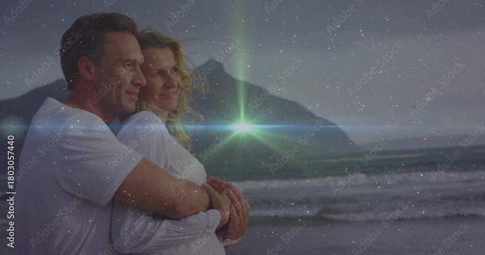 Fototapeta premium Embracing couple wearing white shirts, gazing at dusk horizon on beach with waves, ridge, flare