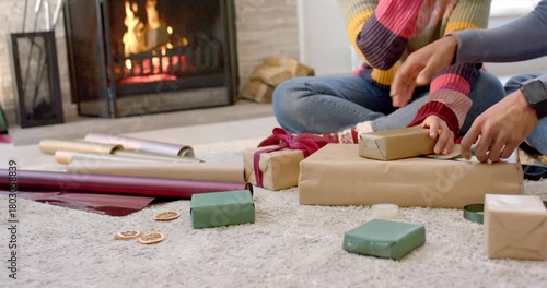 Couple picking up dried orange slice and tying green ribbon while wrapping gift by fireplace