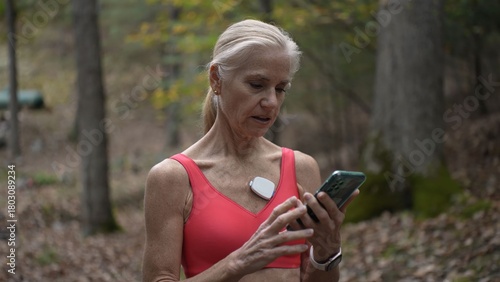 Mature woman engages with heart monitoring technology for atrial fibrillation while walking in a wooded area, promoting health