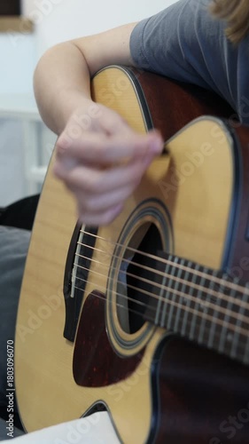 Close-up of teen student strumming acoustic guitar strings during a home practice session, focusing on rhythm training, hand coordination and beginner guitar learning for online music education