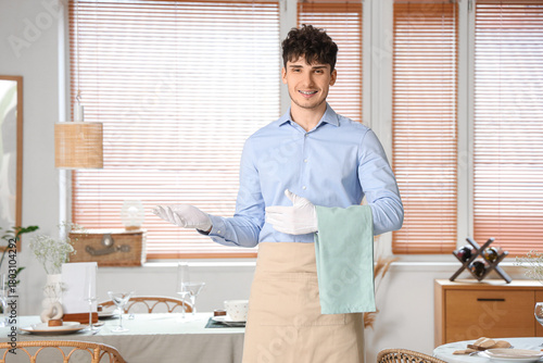 Young waiter with napkin in...