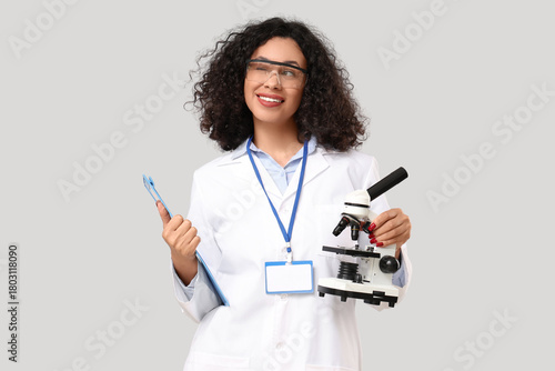 Female African-American scientist with microscope and clipboard on light back...