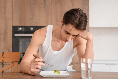 Fotografie Young man with anorexia eating broccoli in kitchen