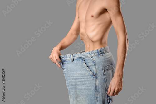 Young man with anorexia in loose jeans on grey background