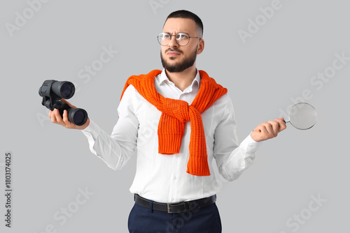 Thoughtful businessman with binoculars and magnifier on light background. Sea...