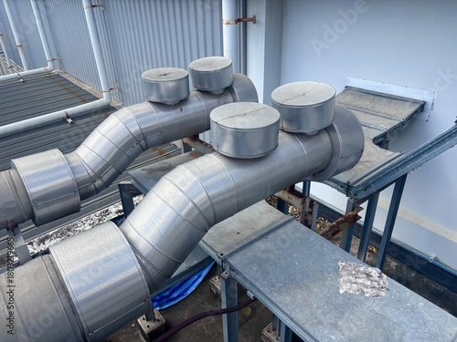 Large, heavily insulated metal pipes and elbows carrying steam or fluid on an industrial rooftop. The piping, mounted on a metal support structure, includes several access points, suggesting