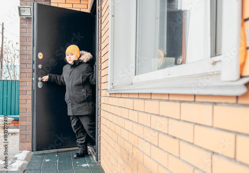 Wallpaper Mural A young Asian boy with a yellow hat stands at the door of a brick house during winter. Snow is visible on the ground outside, child safety on the street Torontodigital.ca