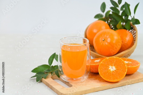 A glass of freshly squeezed orange juice, orange slices with whole oranges, and orange leaves in an organic basket on a white background.