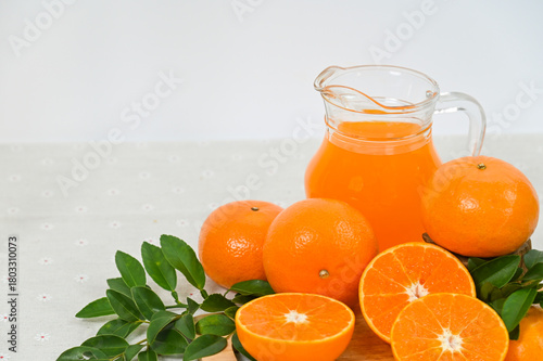 A pitcher of freshly squeezed orange juice, orange slices with whole oranges, and orange leaves, all organic, set against a white background.