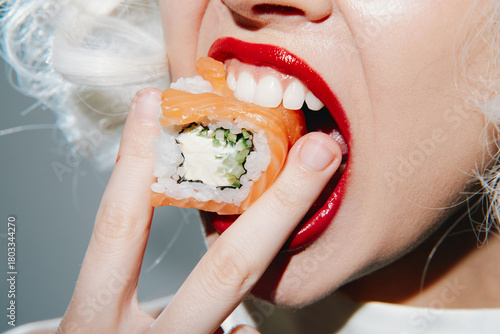 A close-up of a model enjoying sushi with bright red lipstick, showcasing vibrant colors and a playful expression in a contemporary setting.