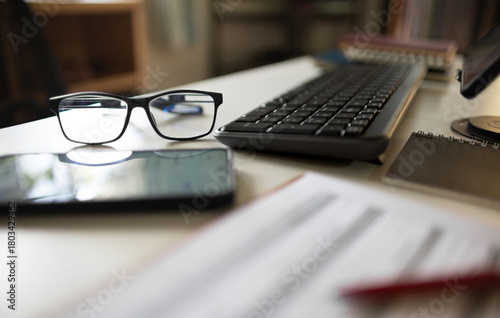 close up shot, eyeglasses with mobile phone, computer keybord, notebook and document on desk office