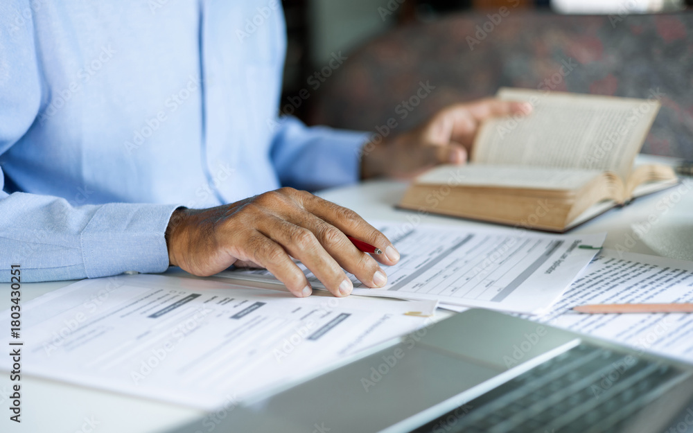 Fototapeta premium asian man checking business document find knowledge in book using laptop to working online via internet technology, close up shot