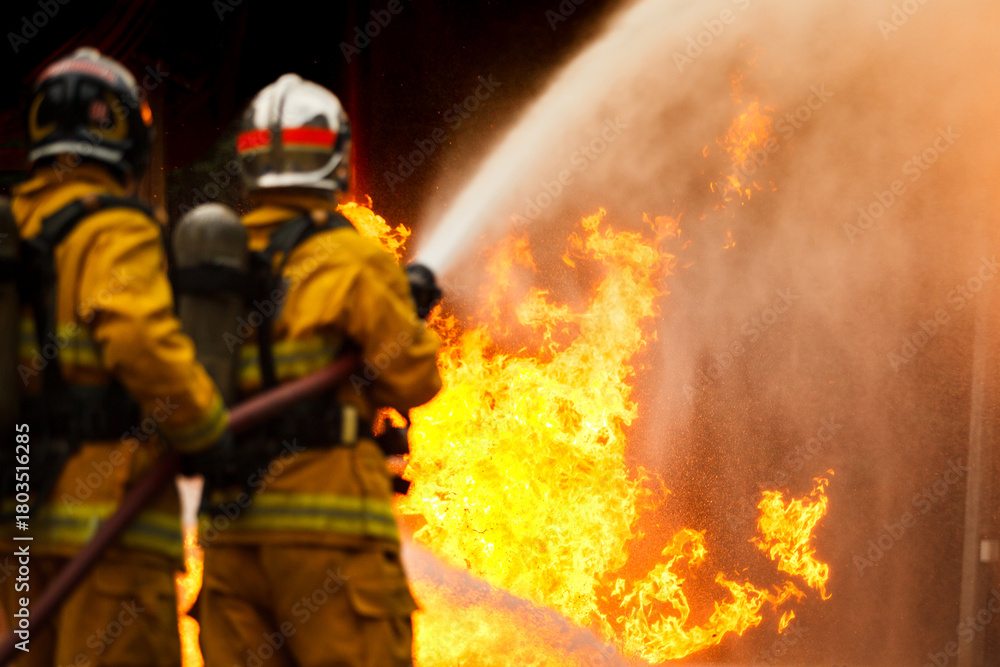 Naklejka premium Firefighters spraying water to control extinguish an intense blaze.