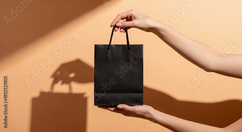 Mockup of a hand holding a plain black shopping bag, soft pastel studio background