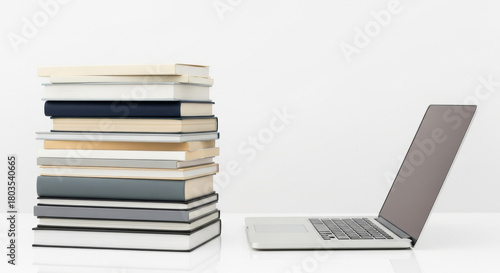 A stack of books sits next to a laptop on a white table against a white backdrop, bathed in bright studio lighting emphasizing education and modern technology.