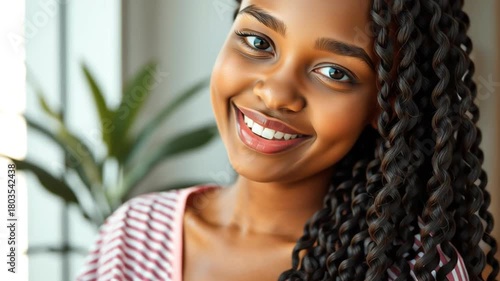 Cheerful happy woman with curly hair and striped shirt, smiling with glowing skin, natural makeup, youthful beauty, joyful expression, indoor portrait